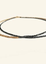 Load image into Gallery viewer, Made from hematite and golden rings, the Hypatia necklace is slender, strong and plays with proportions by simple asymmetry. It can be worn wrapped or long. the combination of gold and dark grey makes this an elegant statement for day and night
