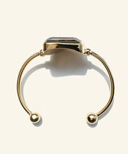 Load image into Gallery viewer, This side view show the oval shape perfectly, designed for comfort the orbs at the ends makes sure there is no digging into the soft underarm. This faceted blue tigereye sits gleaming in a golden encasement. A shimmering dark blue with streaks of gold, makes this stone mysterious and sophisticated. The classic setting and golden colour displays the stone perfectly.