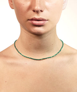 A green emerald necklace is resting on a beutiful neck. We see the bottom half of a face. The image has a white background. With gold lock and chain. The emerald is ruled by Venus, the Goddess of love and beauty, while green activates the heart Chakra. This necklace is the the ultimate confession of self love. 