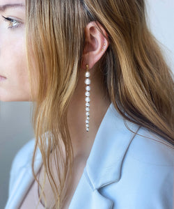 Side profile of woman showing her ear. she's wearing earrings made of graduated white pearls with black knots inbetween them. They're suspended from small domed gold studs. White freshwater pearls  •	Hand-knotted on black silk thread with an 18 ct gold plated silver stud attachment •	Length 8 cm •	Handmade in Australia