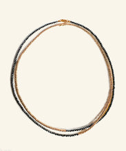 Load image into Gallery viewer, Made from hematite and golden rings, the Hypatia necklace is slender, strong and plays with proportions by simple asymmetry. It can be worn wrapped or long. the combination of gold and dark grey makes this an elegant statement for day and night
