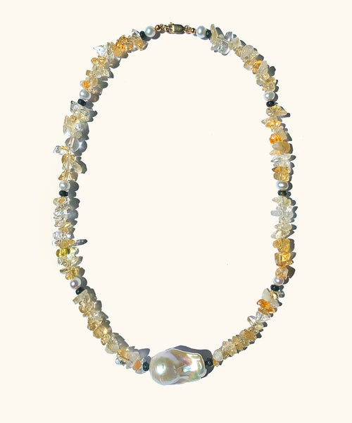 The gleaming white baroque pearl is held in place by a row of sunny Citrine. A necklace strung with light yellow citrine chips. Each 4 cm there is a small white pearl and a black facetted bead. At the bottom of the necklace there is a white organic shaped baroque pearl.