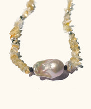 Load image into Gallery viewer, Detail of a white barouque pearl with the citrine necklace in the background. The gleaming white baroque pearl is held in place by a row of sunny Citrine. A necklace strung with light yellow citrine chips. Each 4 cm there is a small white pearl and a black facetted bead. At the bottom of the necklace there is a white organic shaped baroque pearl.
