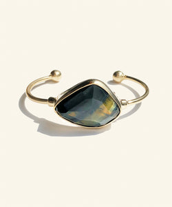 This faceted blue tigereye sits gleaming in a golden encasement. A shimmering dark blue with streaks of gold, makes this stone mysterious and sophisticated. The classic setting and golden colour displays the stone perfectly. The two orbs at the ends adds to comfort. 